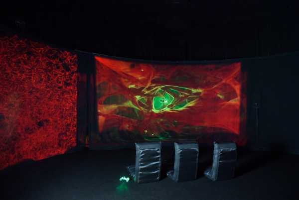 Inside the dark spatial installation, three seats from behind, lighted game controller, animation on screen