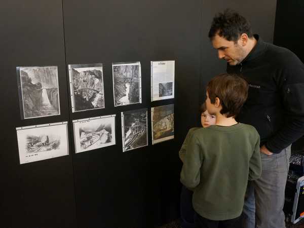 Vater mit Kindern betrachtet Zeitungsartikel an der Wand